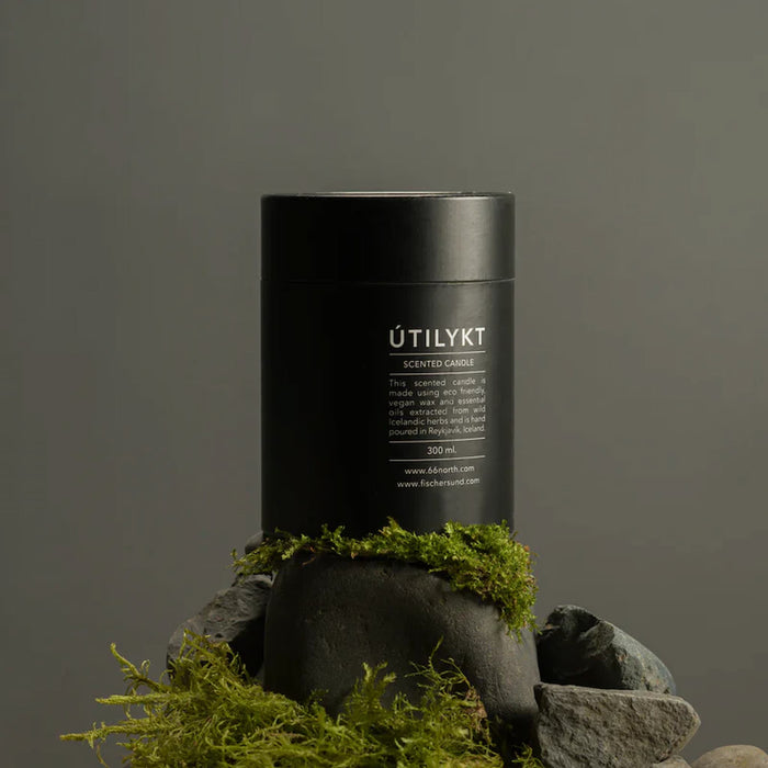 Black cylindrical container labeled 'ÚTILYKT' on a stone surface with green moss, against a dark background.