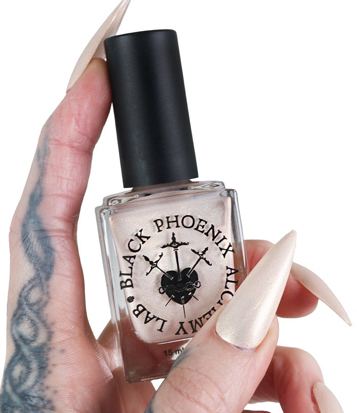 Nail polish bottle held by a hand with long, pointed nails on a white background