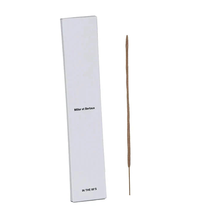 A single incense stick standing vertically next to its tall white rectangular box, which has the text 'Miller et Bertaux' and 'IN THE 80'S' printed on it, set against a white background.