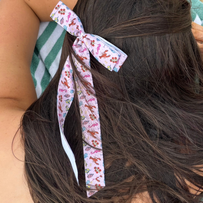 Cococabana sea creature ribbon bow clip secures long brown hair, shown next to a green-striped towel.