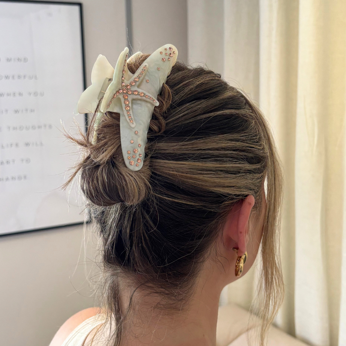 Blonde woman with hair in a bun held by a gold starfish-shaped claw clip decorated with pearls.