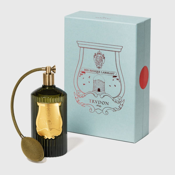 Perfume bottle with gold cap and decorative label next to its packaging box on a light background