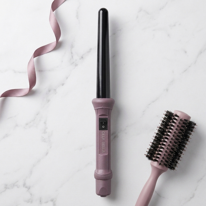 The Olla Bella 1" Ceramic Curling Iron in Plum Metallic shown alongside a matching pink hairbrush on a white marble background with a pink ribbon.