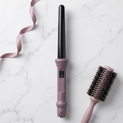 The Olla Bella 1" Ceramic Curling Iron in Plum Metallic shown alongside a matching pink hairbrush on a white marble background with a pink ribbon.