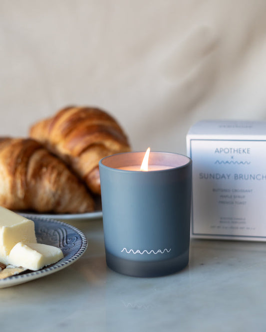 Blue Apotheke candle with white maman logo, in front of white box labeled 'Sunday Brunch', with croissants and butter.
