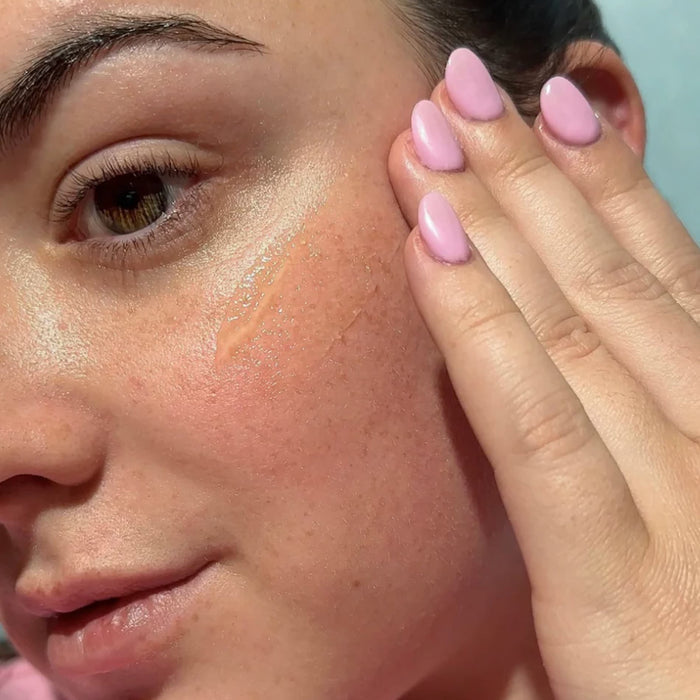 Person applying clear SPF to their cheek with their hand.
