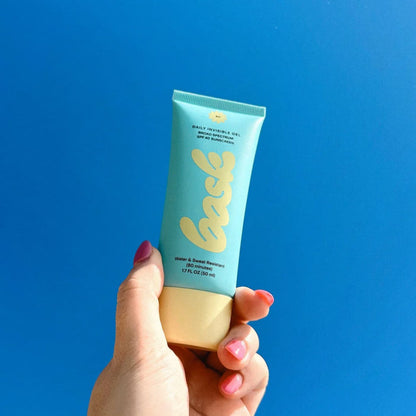 A Bask SPF 40 Face Sunscreen tube held in a hand against a blue sky.