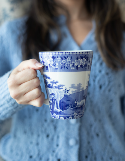 Person holding a blue and white scene patterned mug.