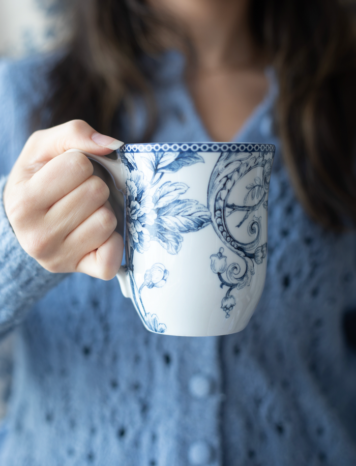 Person holding a blue and white floral mug.