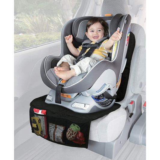 A smiling baby sits in a rear-facing car seat, secured with harness straps. The seat rests on the Nuby Car Seat Protector with Storage Pouch, featuring a non-skid back and mesh pockets for organizing small toys and items below.