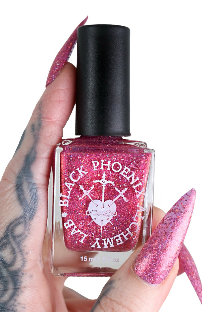 Pink glittery nail polish bottle held by a hand with pink nails on a white background