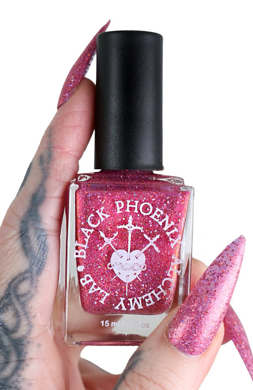 Pink glittery nail polish bottle held by a hand with pink nails on a white background