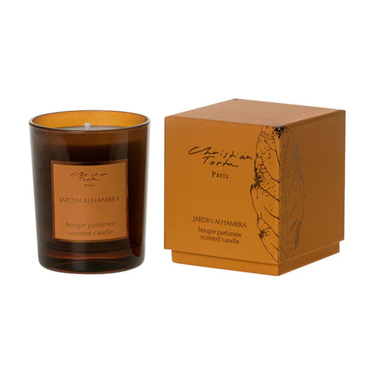 An amber glass scented candle next to its matching packaging, both featuring the brand name Christian Tortu and Jardin Alhambra.