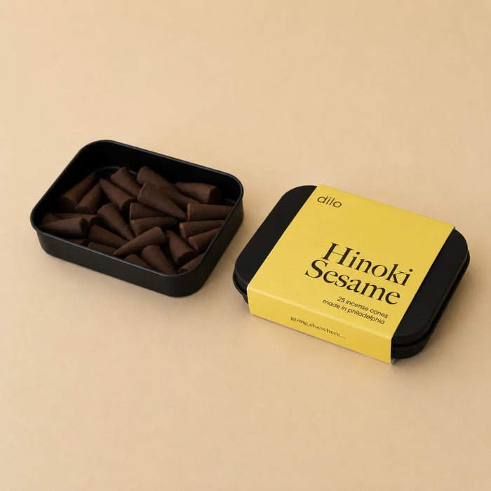 Black container with dilo Hinoki Sesame incense cones and yellow label on a beige background