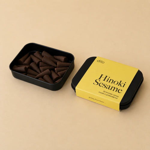 Black container with dilo Hinoki Sesame incense cones and yellow label on a beige background
