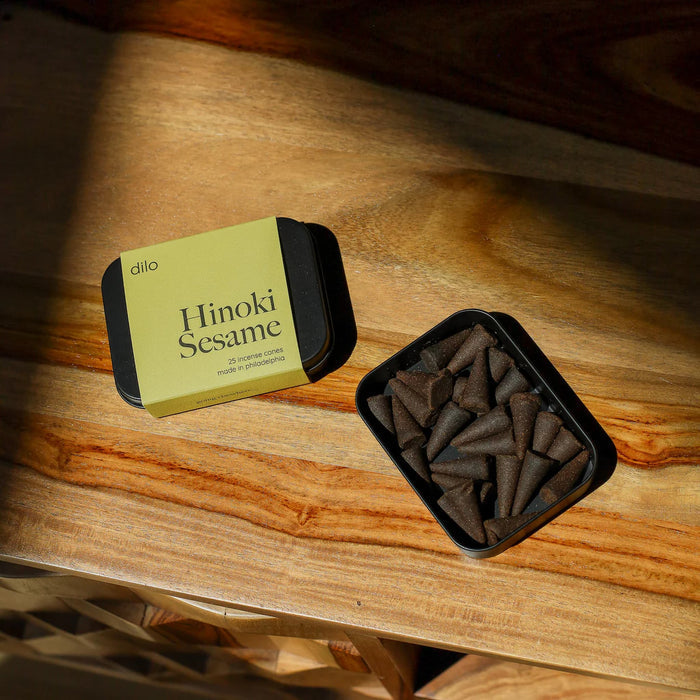 Dilo Hinoki Sesame incense cones in a black container on a wooden surface