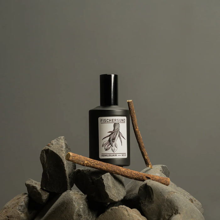 Black bottle of Fischersund 23 room spray with label on a rock against a gray background