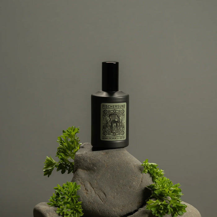 Bottle of Fischersund 101 room spray on a stone surface with greenery against a gray background