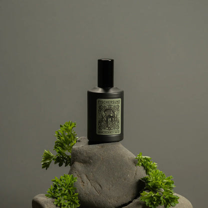 Bottle of Fischersund 101 room spray on a stone surface with greenery against a gray background