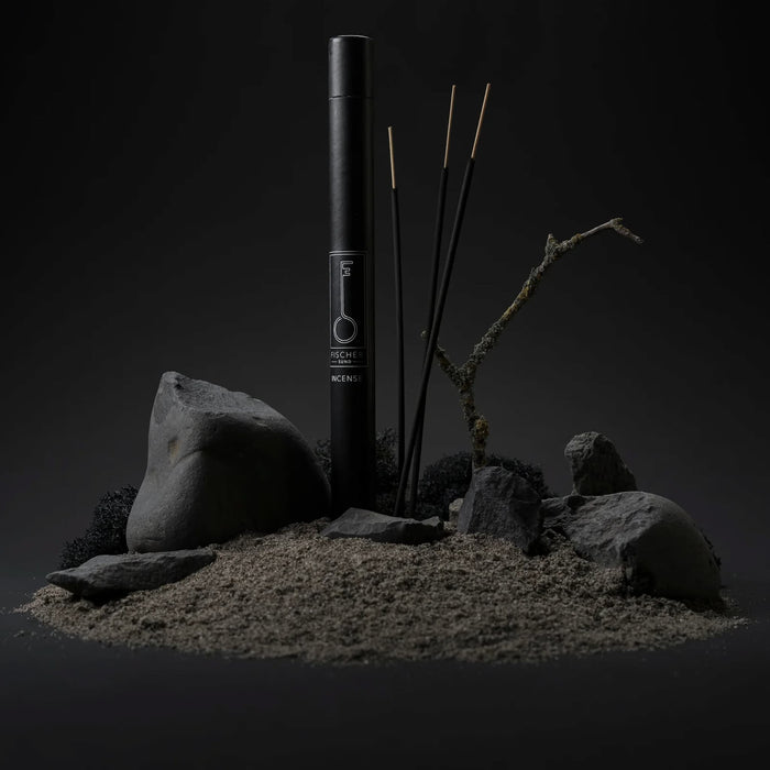 Black cylindrical tube with Fischersund incense sticks and rocks on a dark background