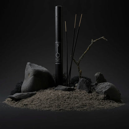 Black cylindrical tube with Fischersund incense sticks and rocks on a dark background