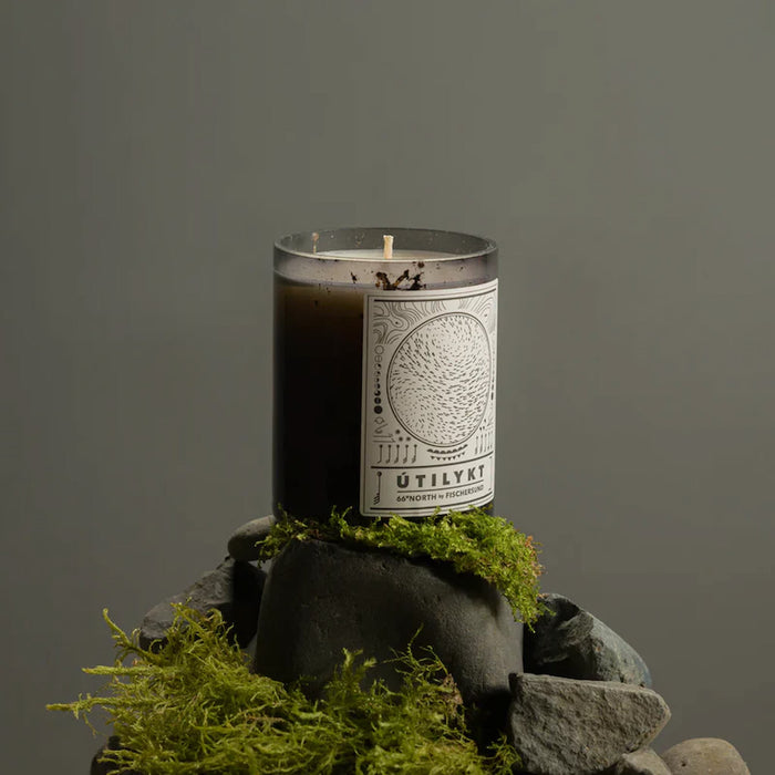 Fischersund Utilykt candle with a label on a stone with moss against a gray background