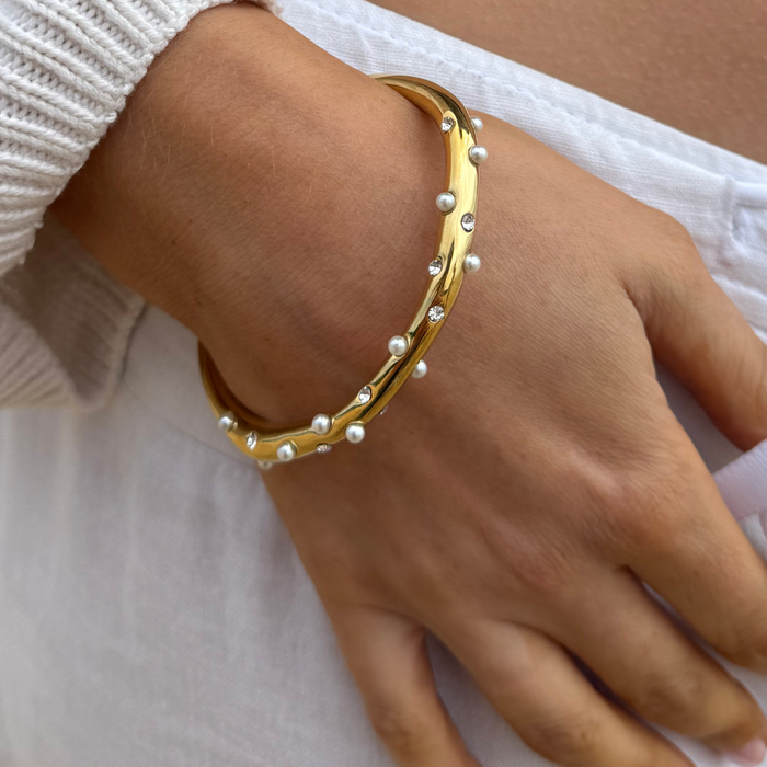 Gold bangle with pearl and crystal accents, displayed on a white background.