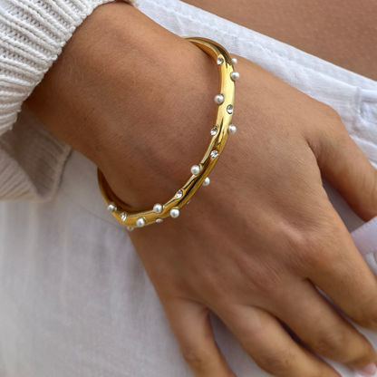 Gold bangle with pearl and crystal accents, displayed on a white background.