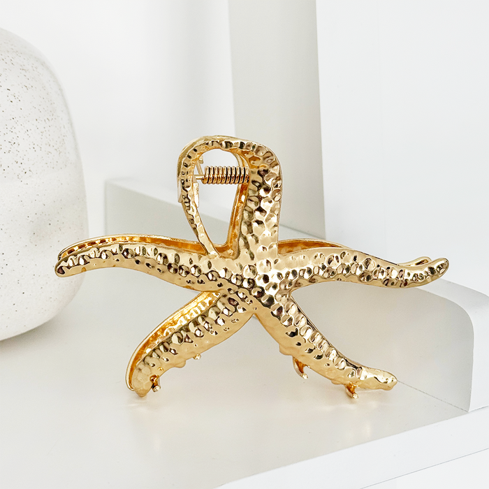 Gold metal starfish-shaped hair claw clip with textured finish on a white background.
