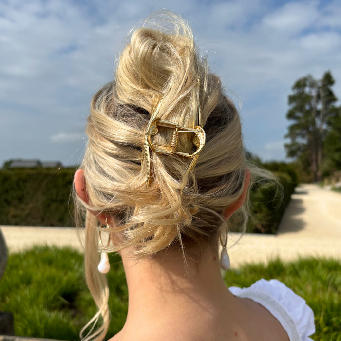 Blonde woman with a loose updo, wearing a gold metal starfish claw clip from Coconut Lane, outdoors in sunlight.