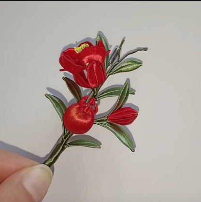 Handcrafted Chanhua thread-wrapped brooch featuring a red flower, green immortal grass leaves, and a blue butterfly with a hanging bead accent.