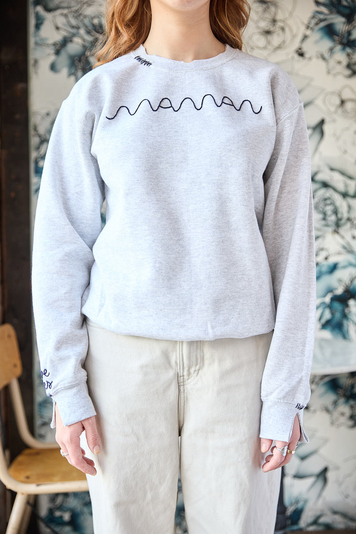 A grey sweatshirt with a blue hand-embroidered 'maman' logo on the front.