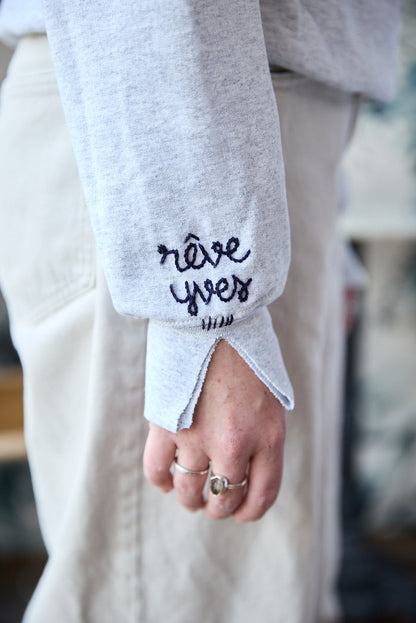 A grey sweatshirt with blue hand-embroidered words on the sleeve.