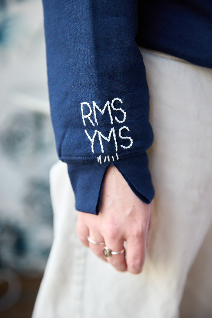 A navy blue sweatshirt with white hand-embroidered initials on the sleeve.
