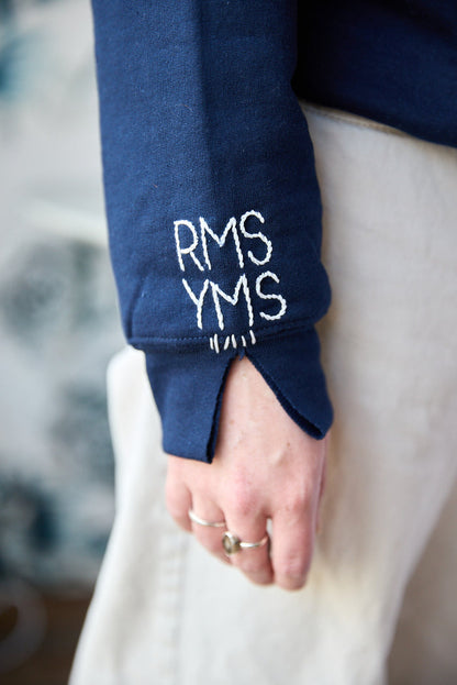 A navy blue sweatshirt with white hand-embroidered initials on the sleeve.