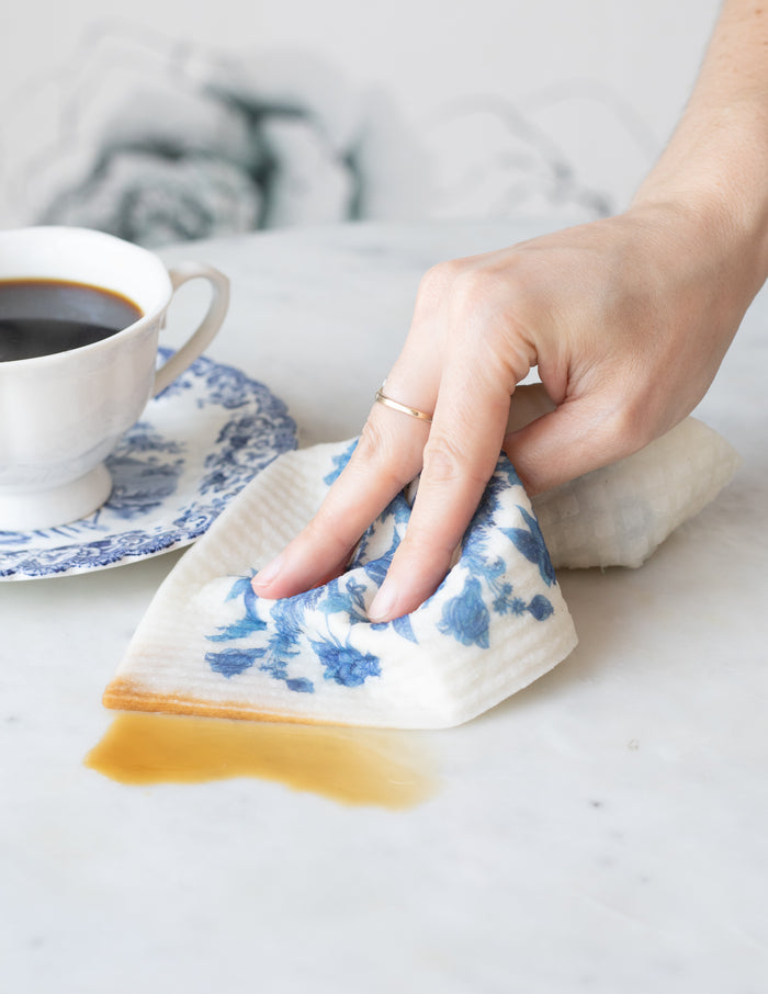 Person wiping a surface with reusable blue-and-white floral dishcloths.