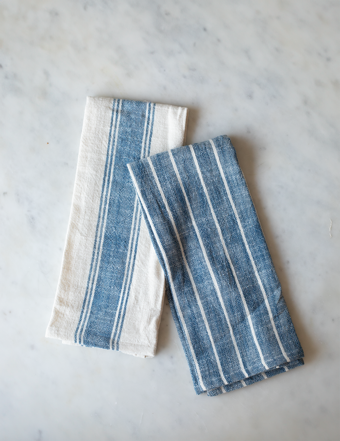 Two folded striped cotton kitchen towels, one with with a blue stripe and the other blue with a white strips.