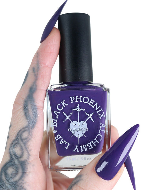 Purple nail polish bottle held by a hand with tattooed fingers on a white background