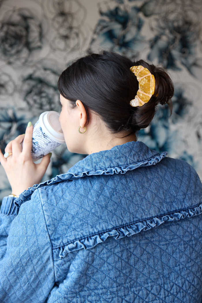 Person wearing a gold croissant-shaped hair clip inspired by French pastry.