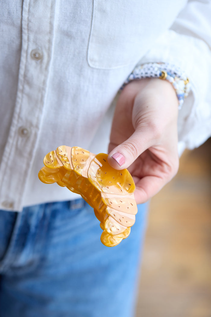 Hand holding a gold croissant-shaped hair clip inspired by French pastry.