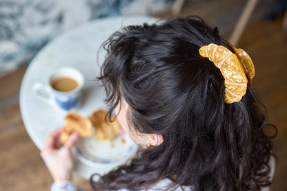 Person wearing a gold croissant-shaped hair clip inspired by French pastry.