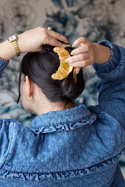 Person clipping a gold croissant-shaped hair clip inspired by French pastry into their hair.