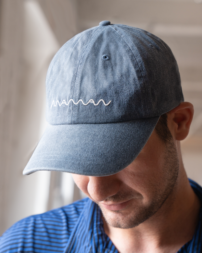 Person wearing a blue denim baseball cap with the 'maman' logo embroidered on the front.