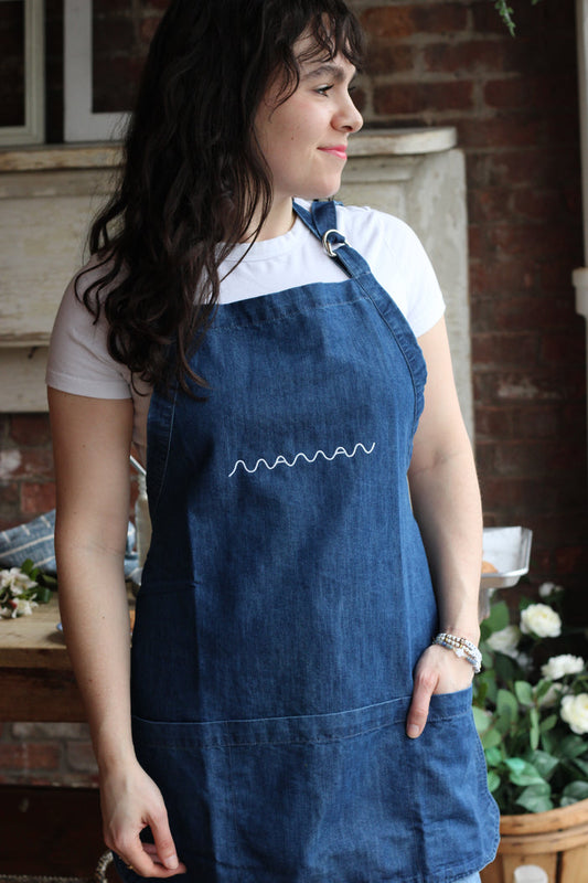 Person wearing a blue denim apron with pockets and the “Maman” logo embroidered on it.