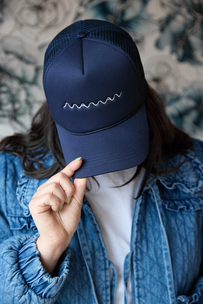 Person wearing a navy blue trucker hat with white "maman" logo embroidered and a mesh back.