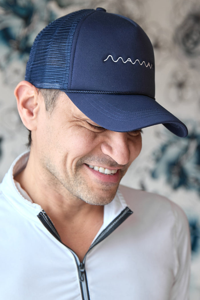 Person wearing a navy blue trucker hat with white "maman" logo embroidered and a mesh back.