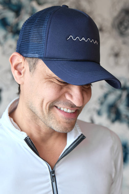 Person wearing a navy blue trucker hat with white "maman" logo embroidered and a mesh back.