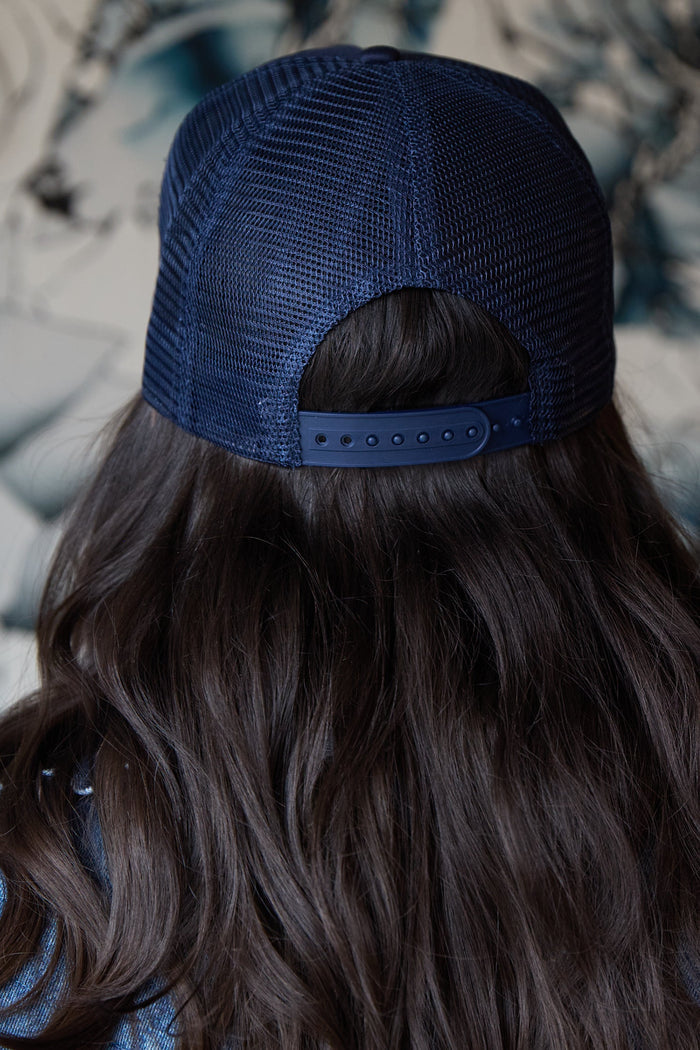 Person wearing a navy blue trucker hat with mesh back.