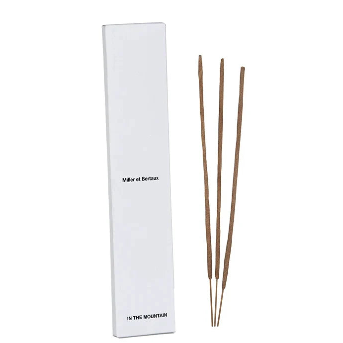 A tall white rectangular box labeled 'Miller et Bertaux' and 'IN THE MOUNTAIN' stands beside three incense sticks white background.