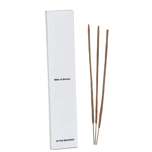 A tall white rectangular box labeled 'Miller et Bertaux' and 'IN THE MOUNTAIN' stands beside three incense sticks white background.